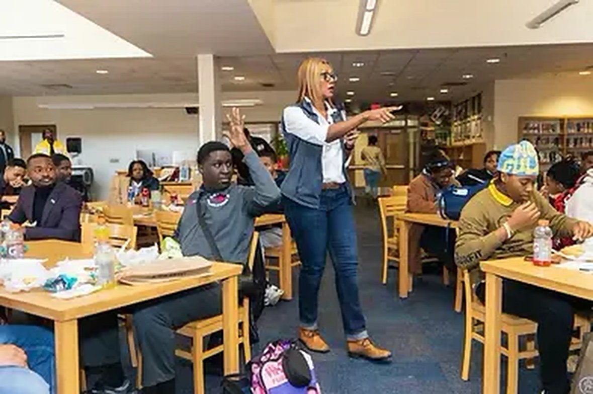 A facilitator leading a Financial Foundations™ session with students at tables in a school cafeteria